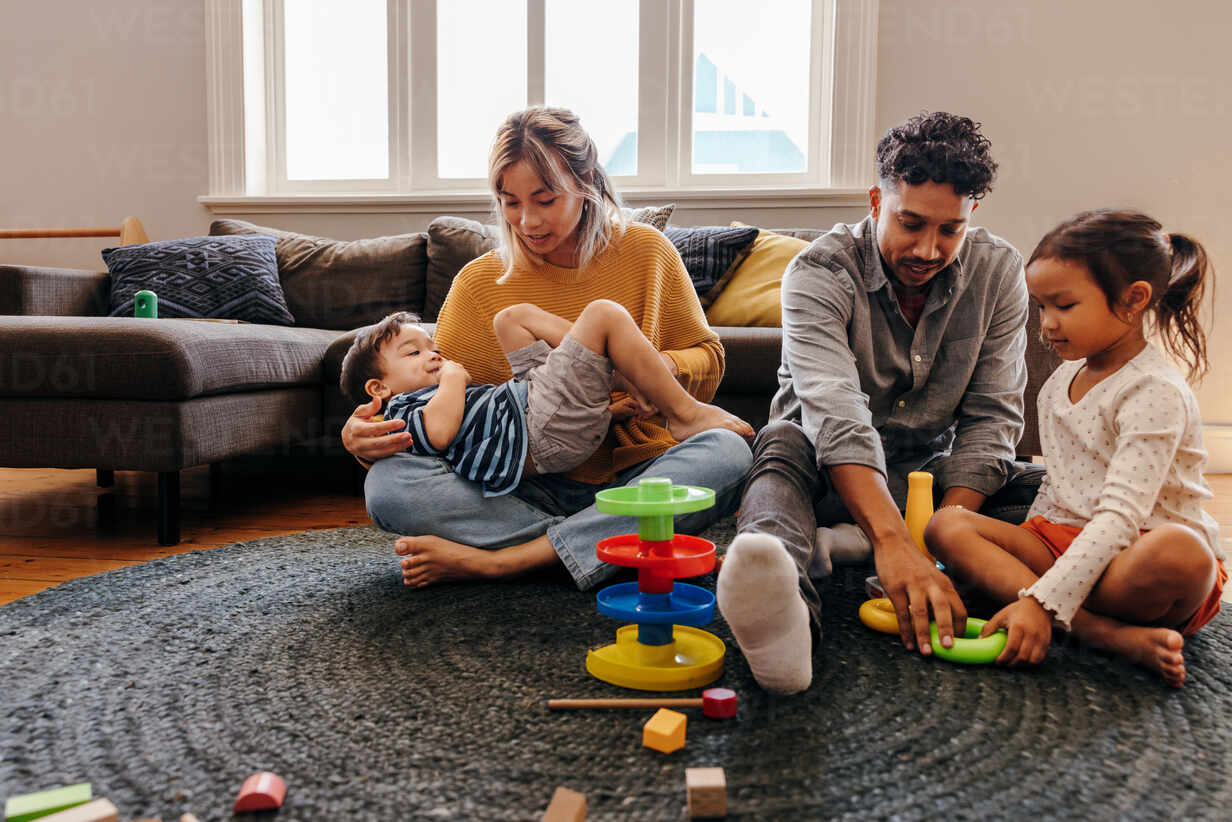 mom and dad playing with their kids in the living room at home two young parents having fun with their son and daughter during playtime family of four spending some quality time together JLPSF11335
