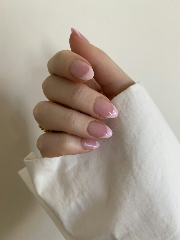 Close-up of hand with glossy pink almond-shaped nail manicure