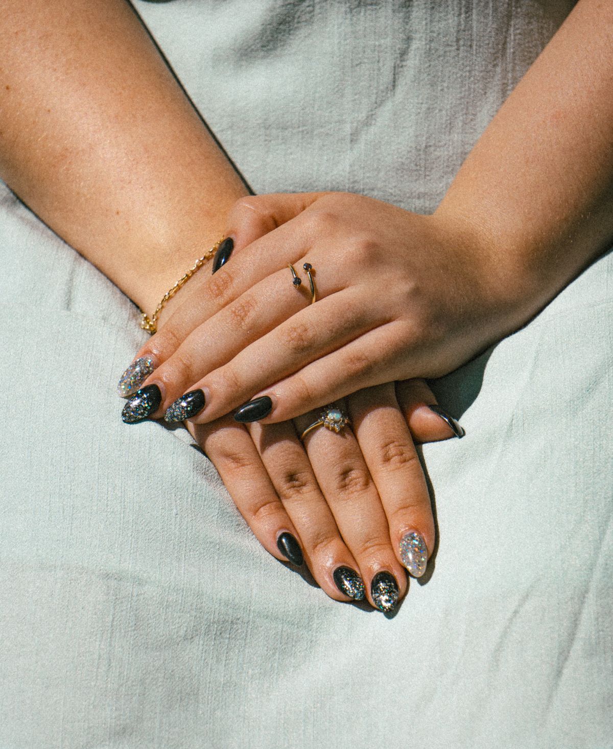 Hands with black and silver chrome nail art wearing rings in sunlight