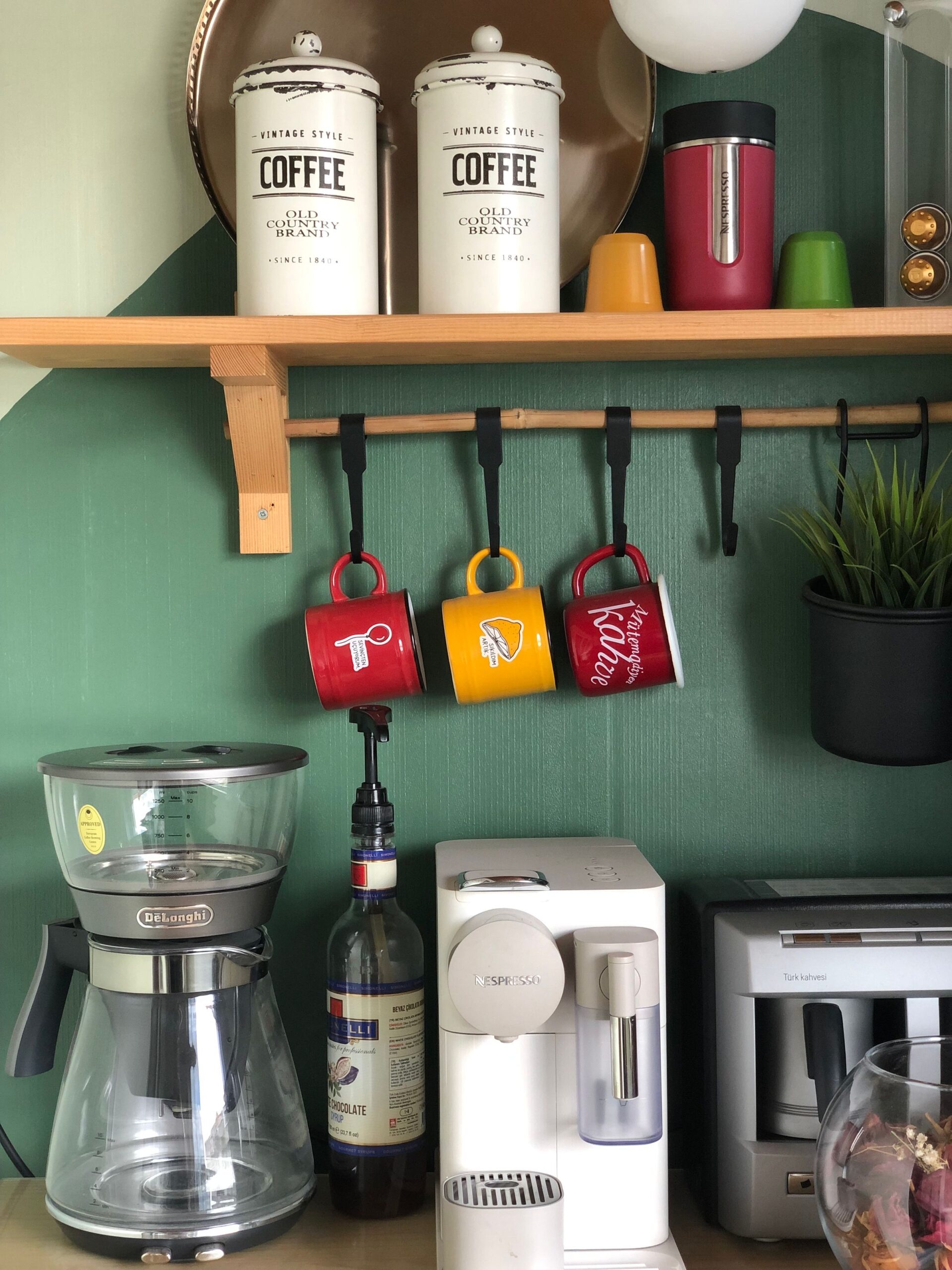 Home Coffee Bar Ideas That Feel Like a Real Café Corner 7 Coffee station with colorful mugs hanging on hooks below a shelf with coffee canisters
