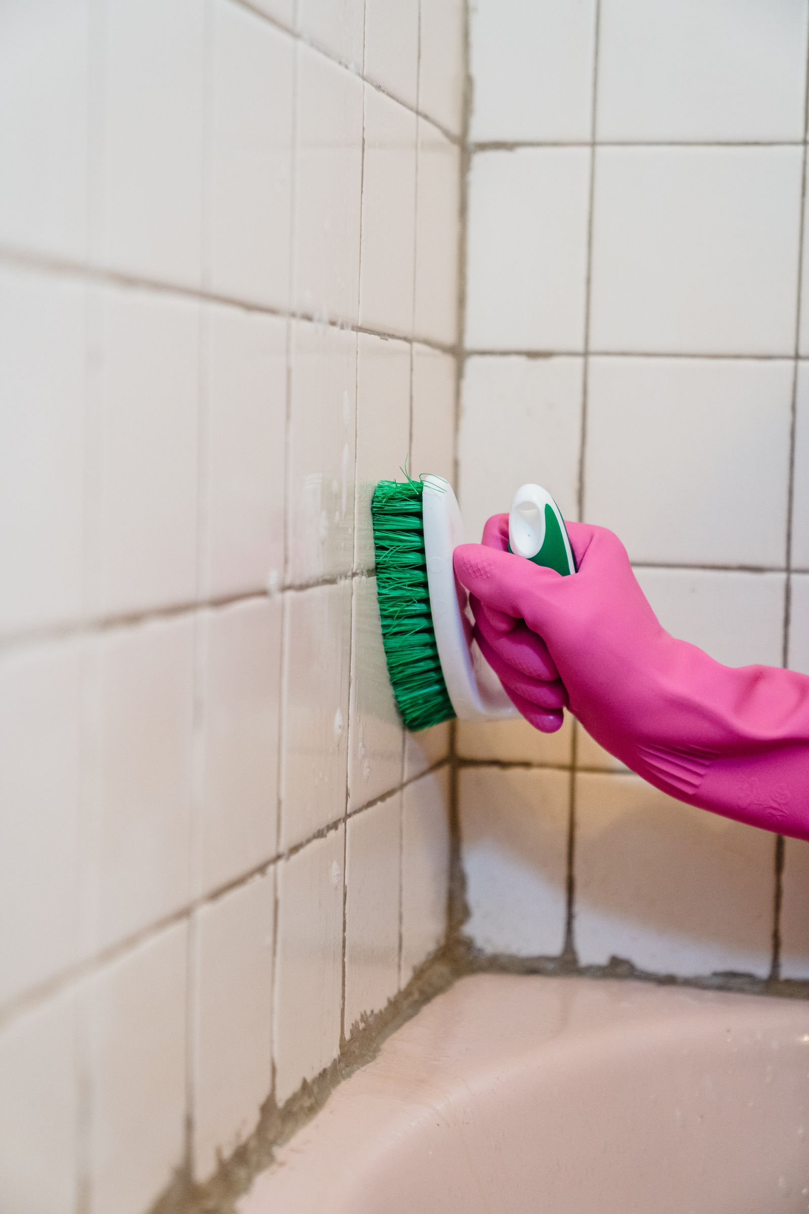 Gloved hand scrubbing bathroom tile grout