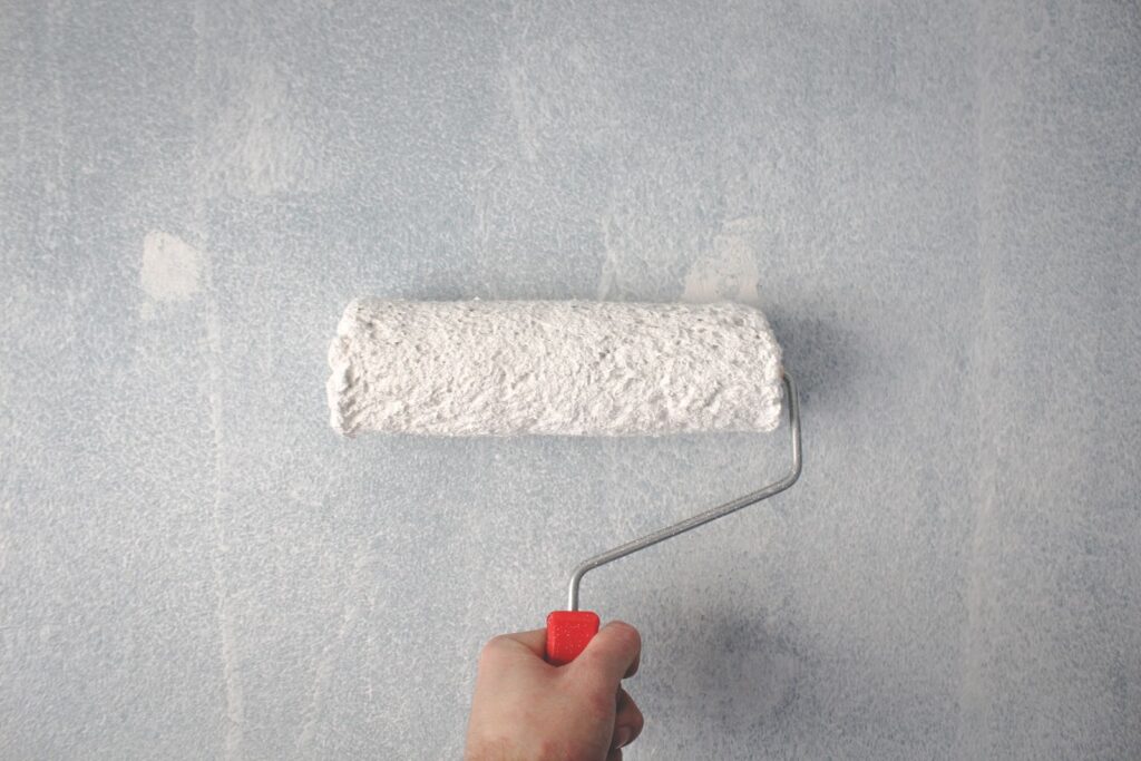 Person applying fresh paint to a wall with a roller