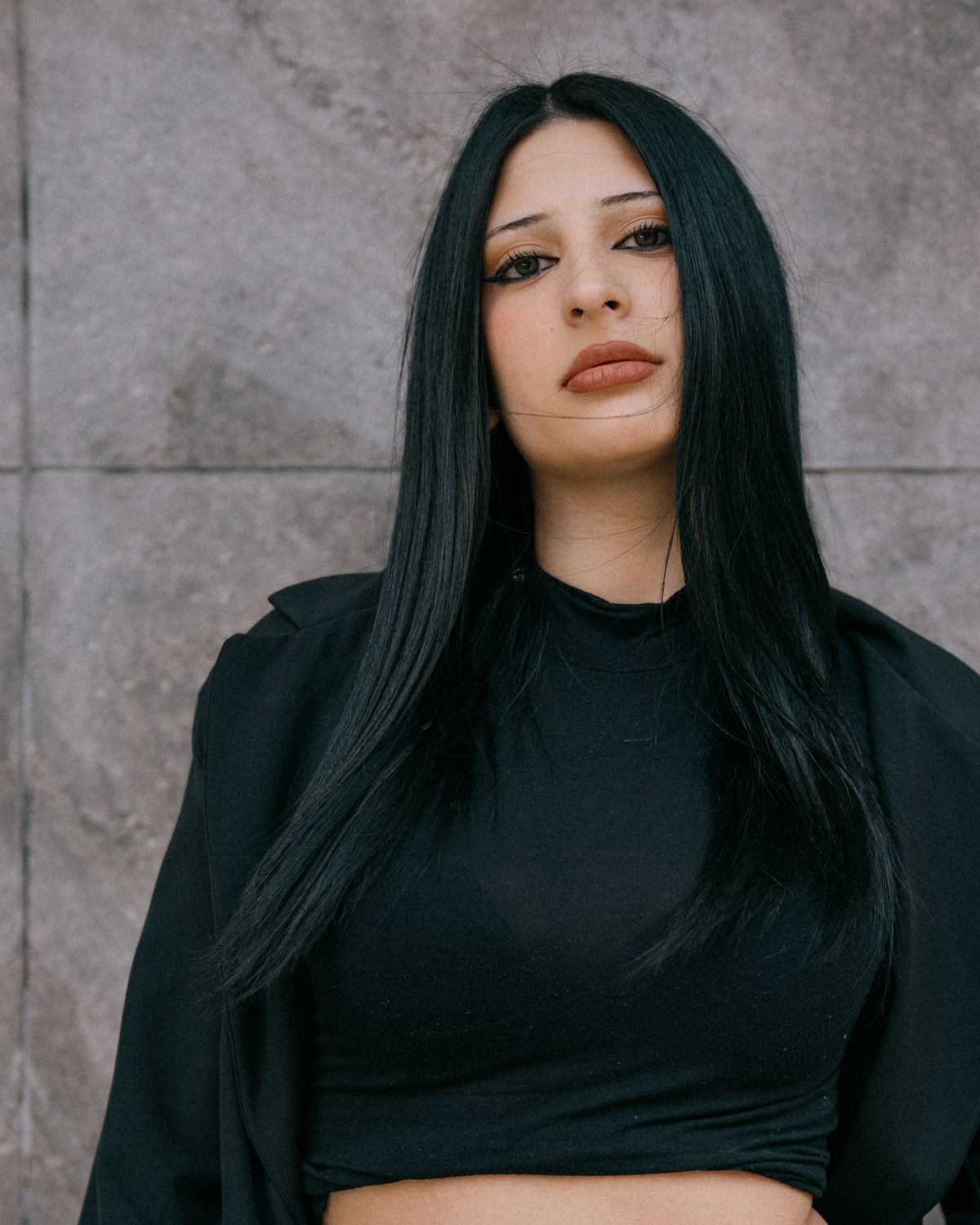 The Elegance of Jet Black Hair Color for Women 2 Woman with long black hair posing against a stone wall