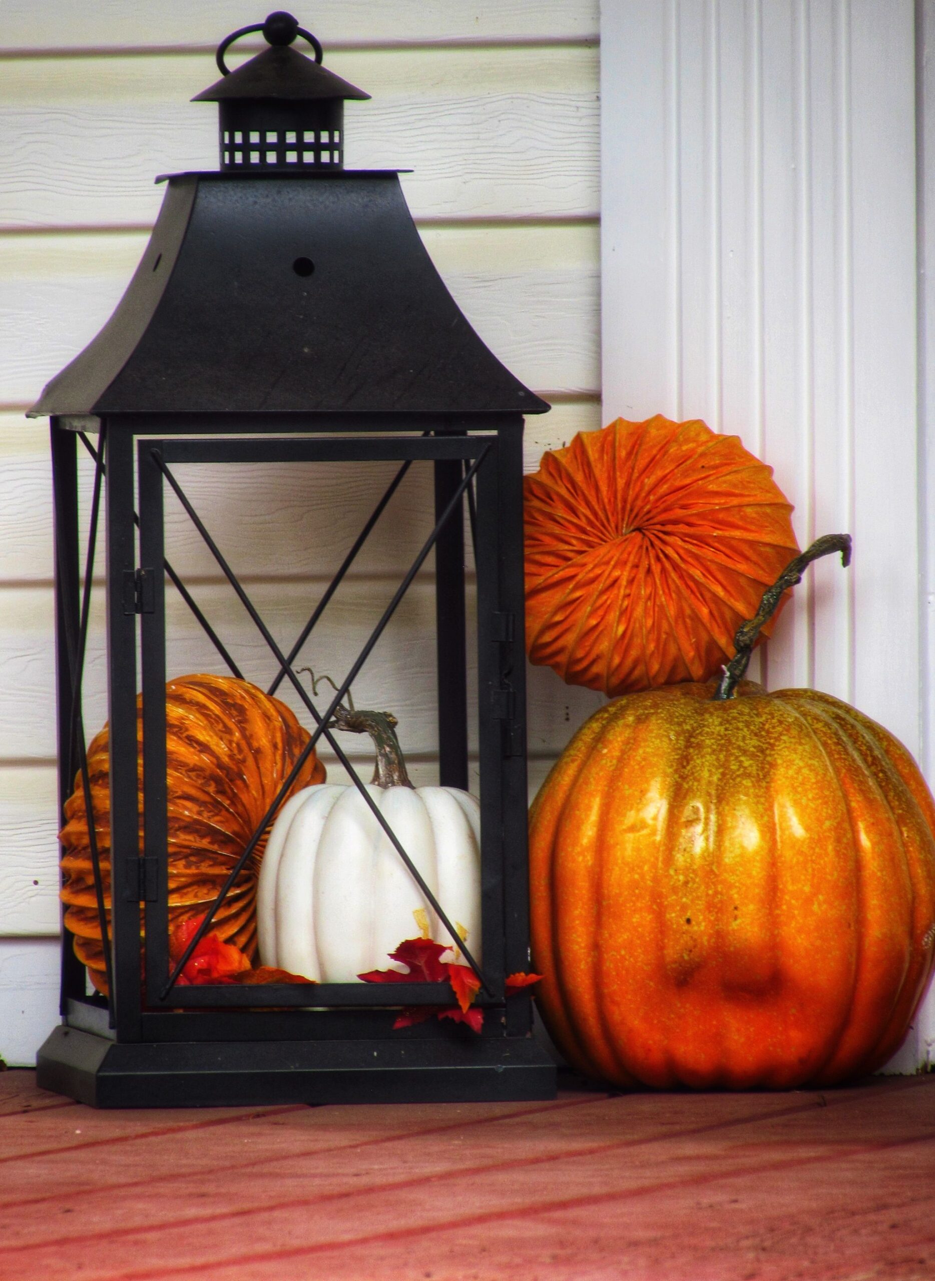 Decorative black lantern with mini pumpkins against porch siding, photo by Leslie Beasley via Pexels