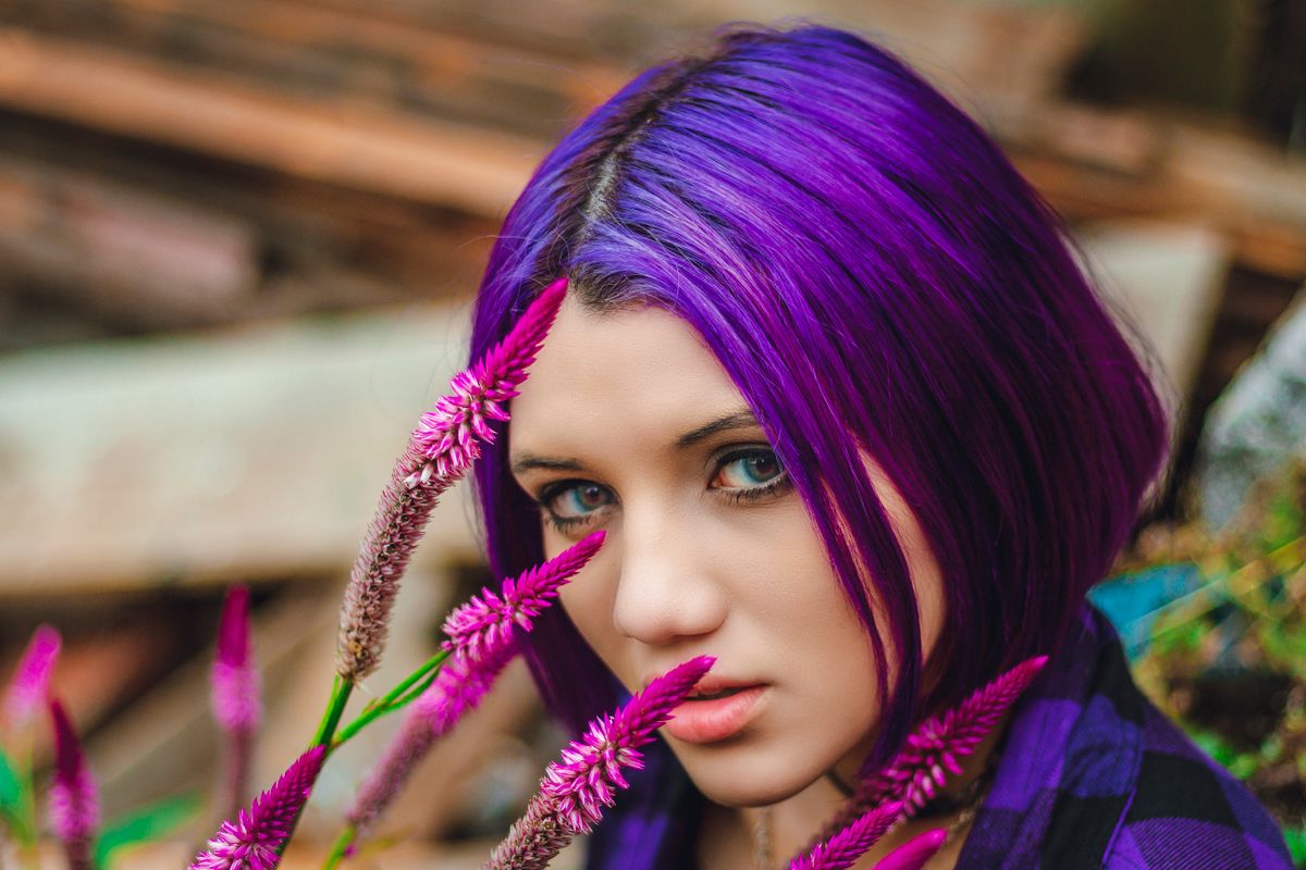Woman with purple hair among vibrant flowers