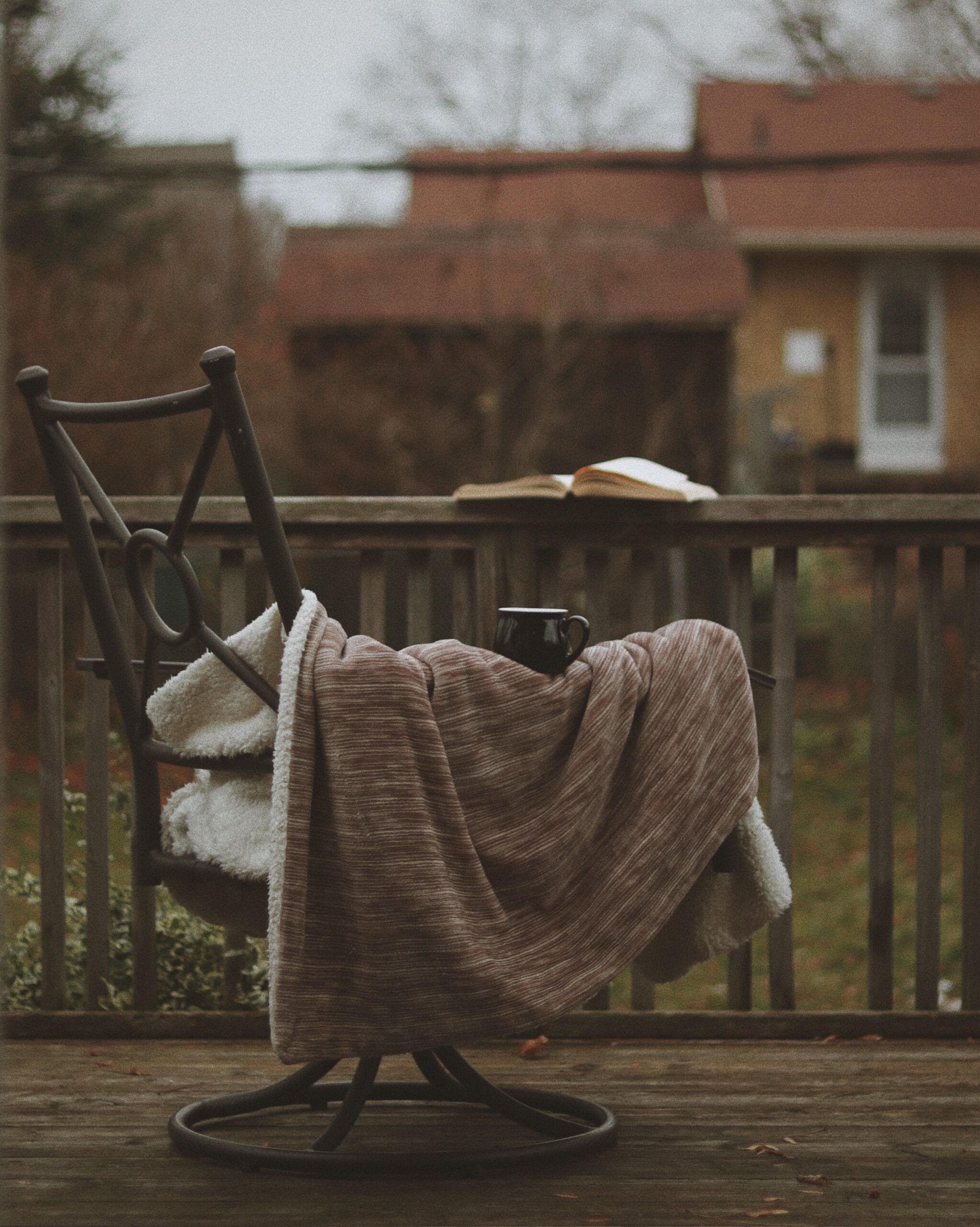 Cozy porch chair with a knit blanket, mug, and open book, photo by Dalia Al-Refai via Pexels