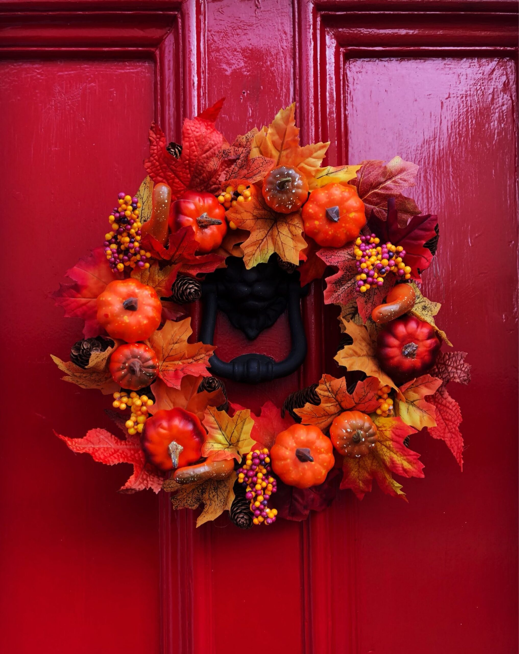 Autumn wreath with pumpkins and fall leaves on a red front door, photo by FJ Robertson via Pexels